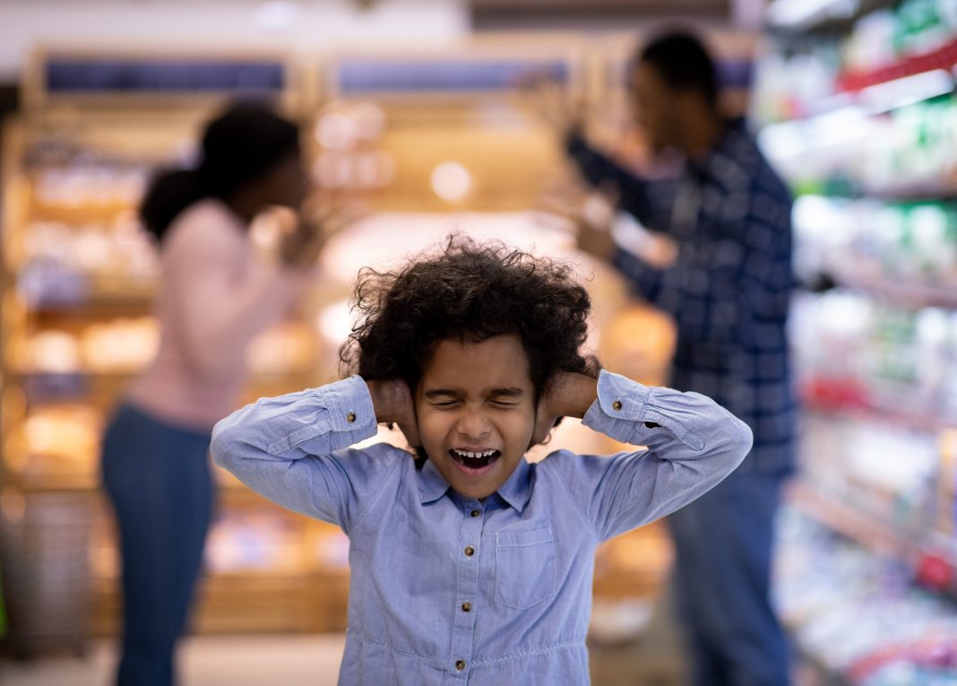 Little black girl covering her ears and shouting while her parents arguing at supermarket